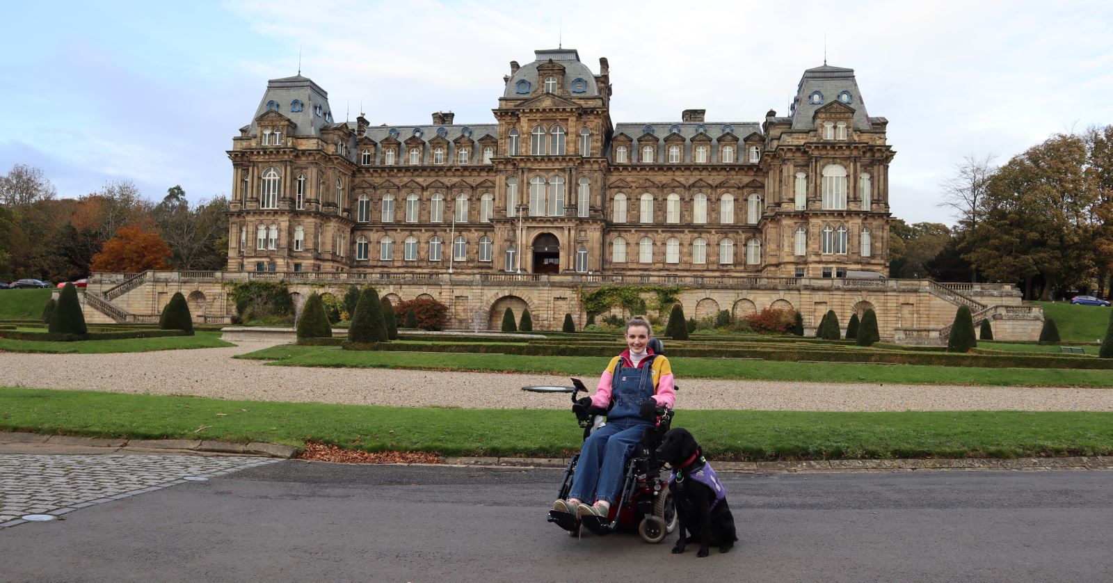 kate Stanforth sat in her wheelchair with support dog in the grounds of The Bowes Museum, with the museum in the background. 